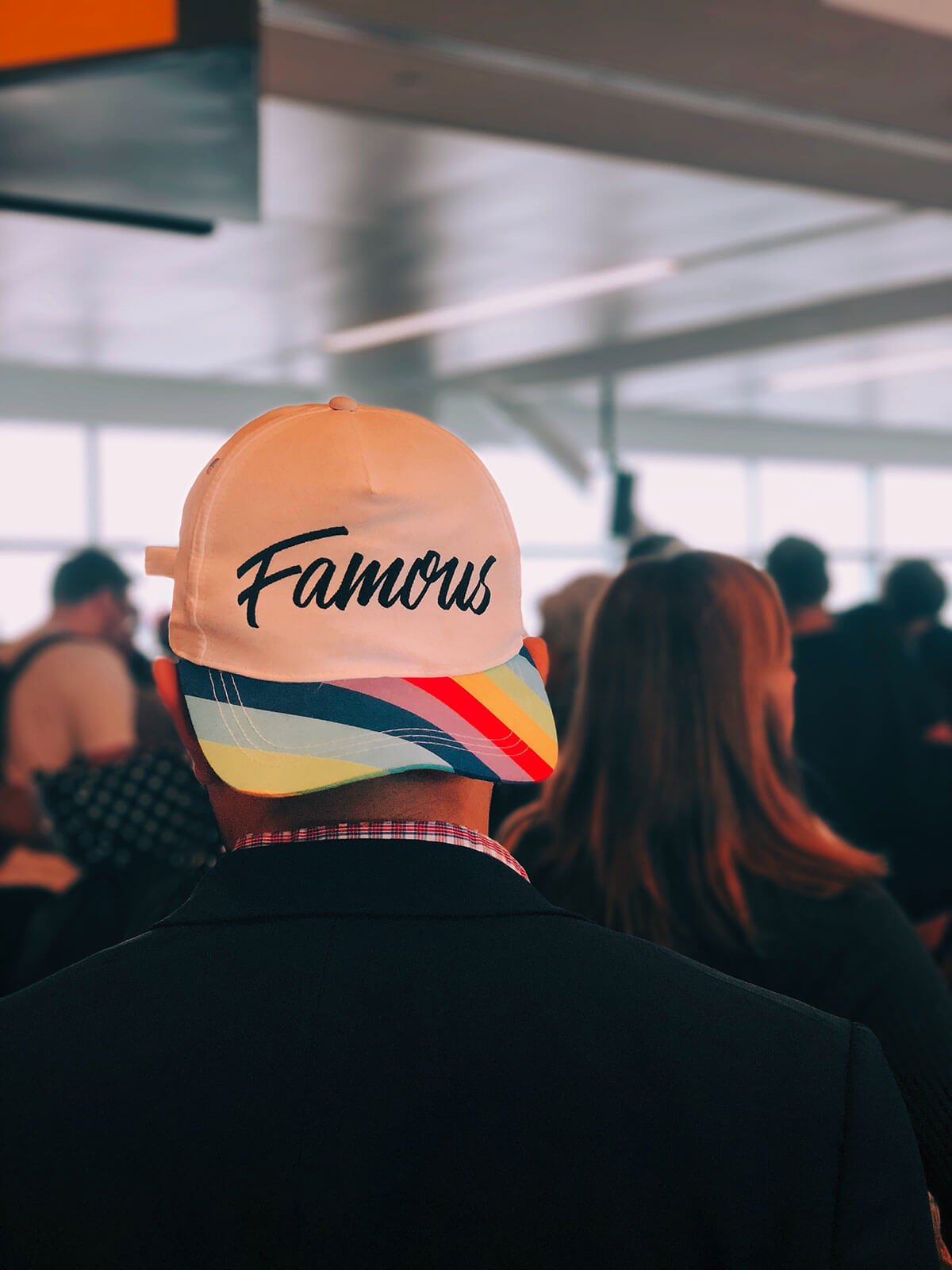 Man in a crowd wearing a white hat with the word 'Famous' printed on it.