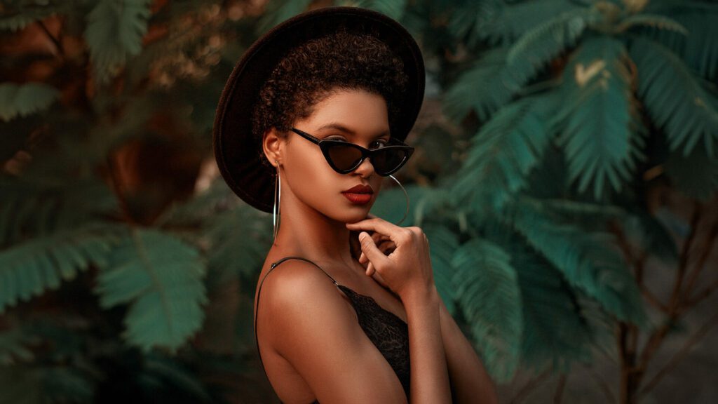 Black woman models with fashionable hat and sunglasses in front of jungle