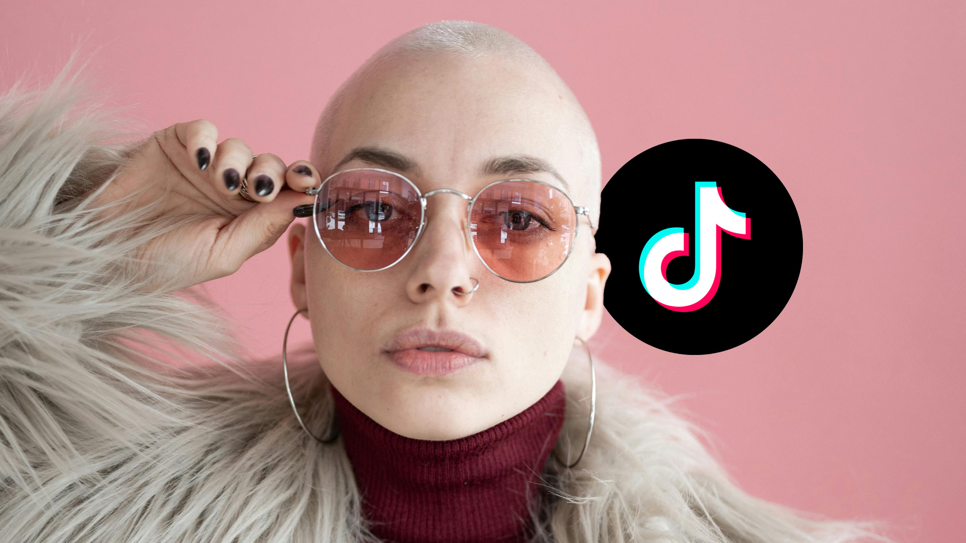 A content creator poses in a faux fur coat, maroon turtleneck and rose colored glasses' TikTok logo